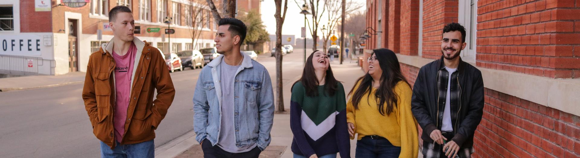 Five college students walking down a sidewalk